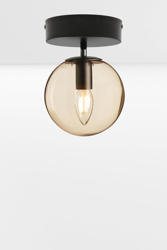 Glass orb shade with an amber finish on a black flush mount, using a candle bulb.
