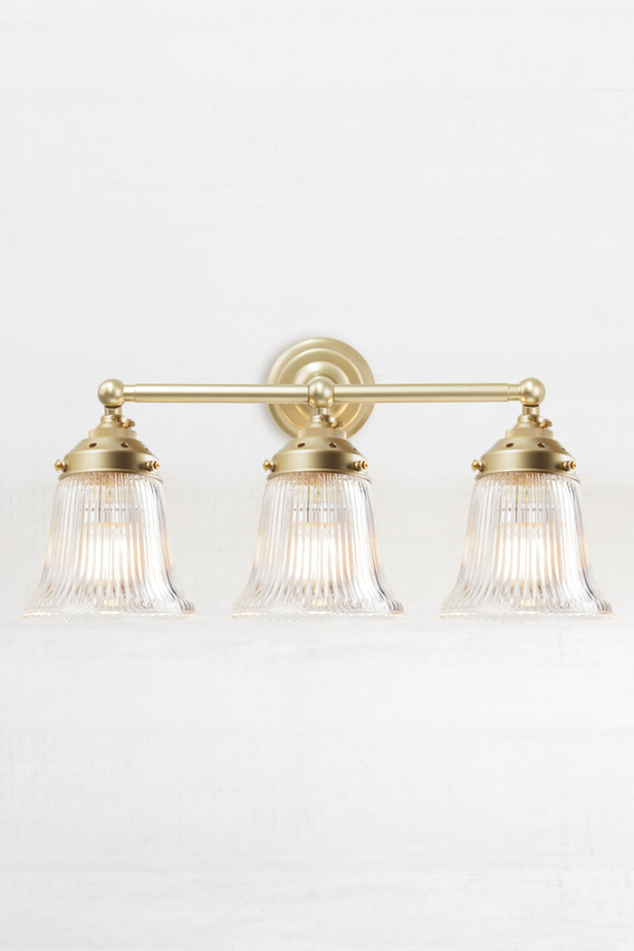 Front facing triple gold/brass wall sonce with clear reeded glass shades.
