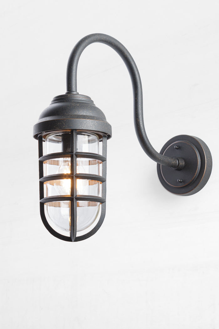 Nautical designed wall light with an antique bronze finish, cage and glass guard- no shade.