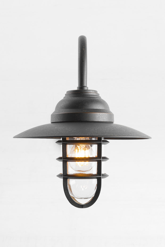 Front view of the antique brass wall light with shade, cage and glass guard and clear A60 bulb.