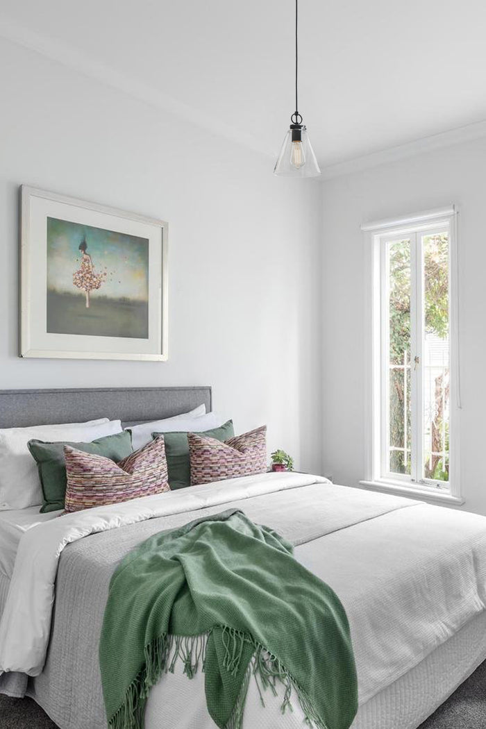 Large glass coe shade with black hardeware in a white and green bright bedroom.
